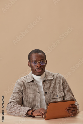 Portrait of African man in eyeglasses looking at camera sitting at the table with digital tablet