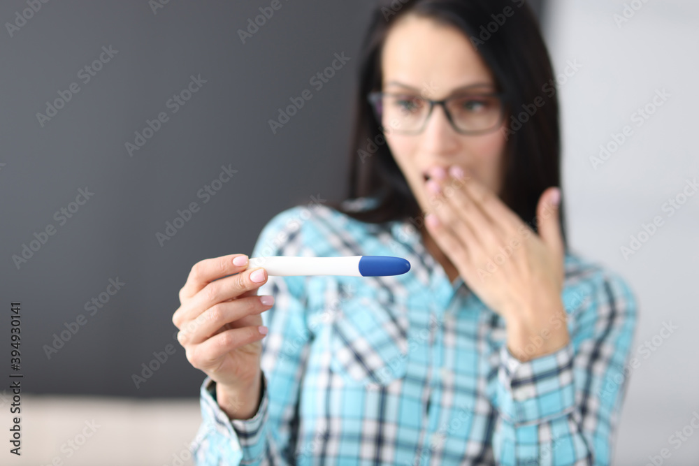 Surprised young woman covering her mouth with hand and looking at test at home. Pregnancy diagnosis test concept Surprised young woman covering her mouth with hand and looking at test at home. Pregnancy diagnosis test concept