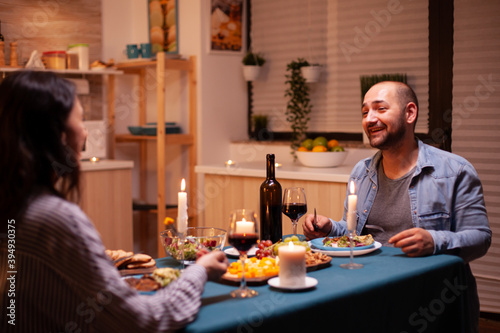 Husband telling a story to wife in kitchen during festive dinner. Relax happy people  sitting at table in kitchen  enjoying the meal  celebrating anniversary in the dining room