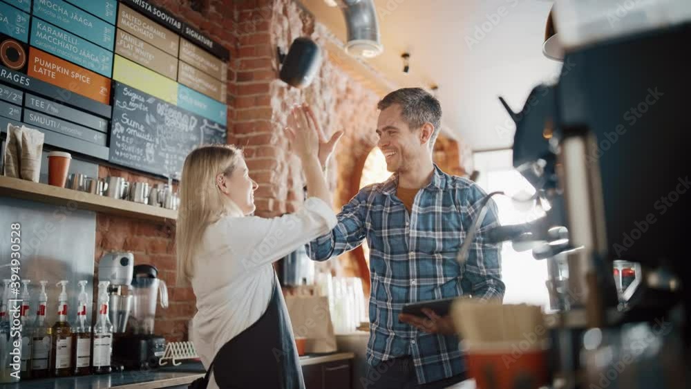 Two Diverse Entrepreneurs Have a Team Meeting in Their Stylish Coffee Shop. Barista and Cafe Owner Discuss Work Schedule and Menu on Tablet Computer. Young Female and Male Give Each Other High Five.