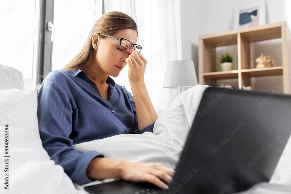 technology, remote job and people concept - tired or stressed young woman in glasses with laptop computer working in bed at home bedroom technology, remote job and people concept - tired or stressed young woman in glasses with laptop computer working in bed at home bedroom