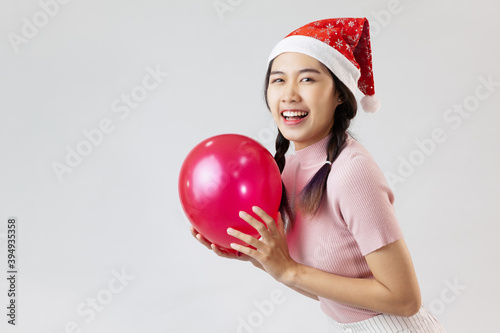 Portrait of young asian woman wearing a santa hat. Holding a balloon and smiling. On white background © CREATIVE WONDER