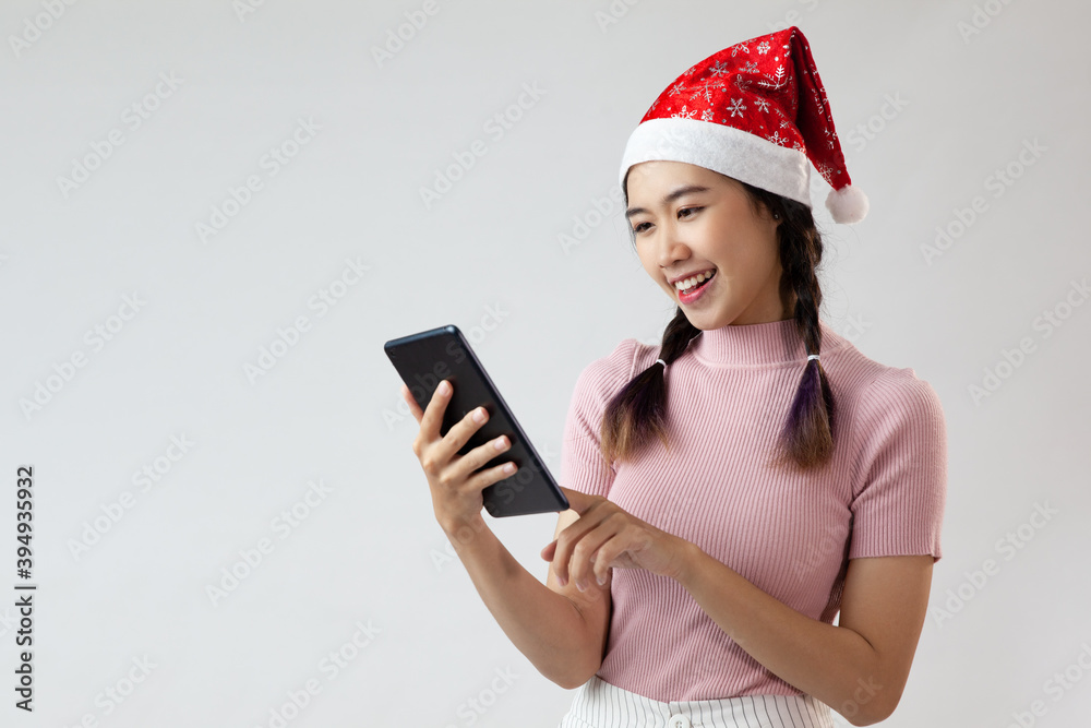 cute asian woman wearing a santa hat, looking a tablet and smile on a white background cute asian woman wearing a santa hat, looking a tablet and smile on a white background