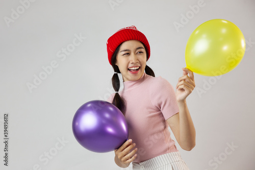 Portrait of cute asia woman wearing a red wool hat. Holding a balloon and smiling. On white background © CREATIVE WONDER