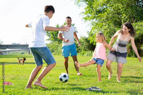 Group of smiling children and parents having fun together outdoors playing football. High quality photo