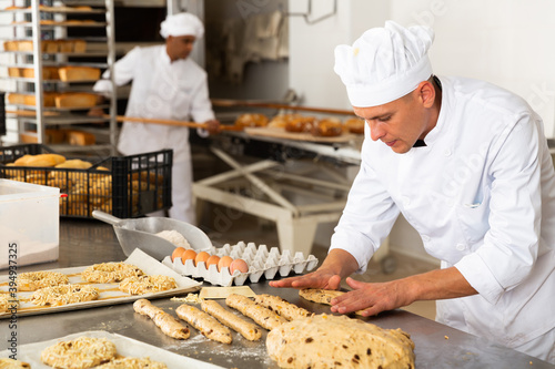 Obraz na plátně Portrait of man baker working with dough and forming baguettes