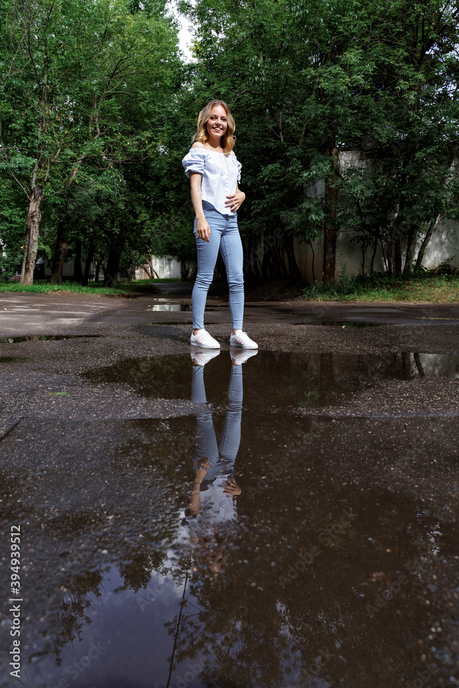 beautiful blonde girl on a sunny summer day after the rain. female reflected in a large puddle