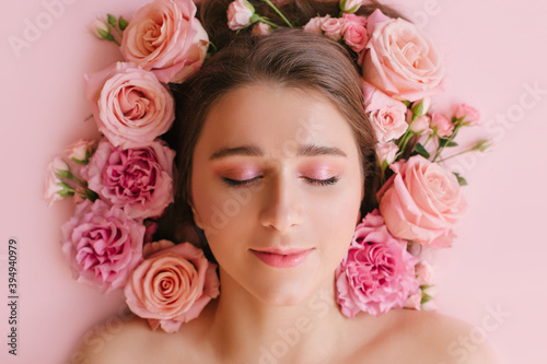 Close up portrait of beautiful woman face wih bright make up and perfect skin posing with roses on pink background. © polinaloves
