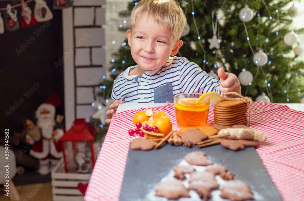 boy near the christmas tree eats cookies and drinks tea