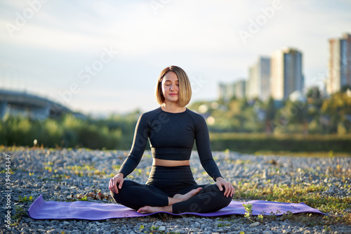 calm young caucasian woman is meditating in lotus pose outdoors, sit with eyes closed, alone on fresh air, wearing sportswear © Roman