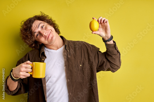 It's cold and emidemic outside happy attractive guy enjoying fresh aromatic tea with lemon, isolated on yellow background, smile photo