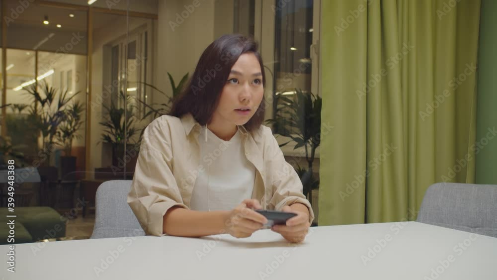 Excited beautiful pro gamer asian woman in casual clothes wearing earphones, streaming and playing online video games on computer , talking and sharing tips with fans while sitting in coworking space. Excited beautiful pro gamer asian woman in casual clothes wearing earphones, streaming and playing online video games on computer , talking and sharing tips with fans while sitting in coworking space.