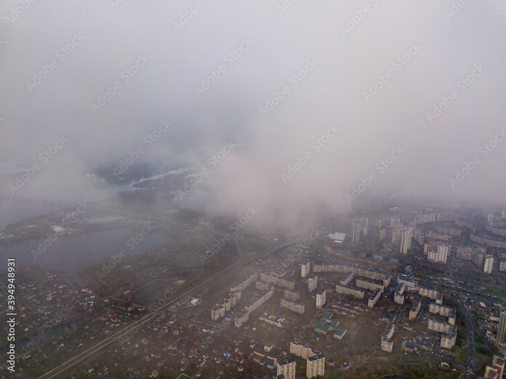 High aerial flight in the clouds over Kiev. An autumn cloudy morning, the Dnieper River is visible on the horizon.