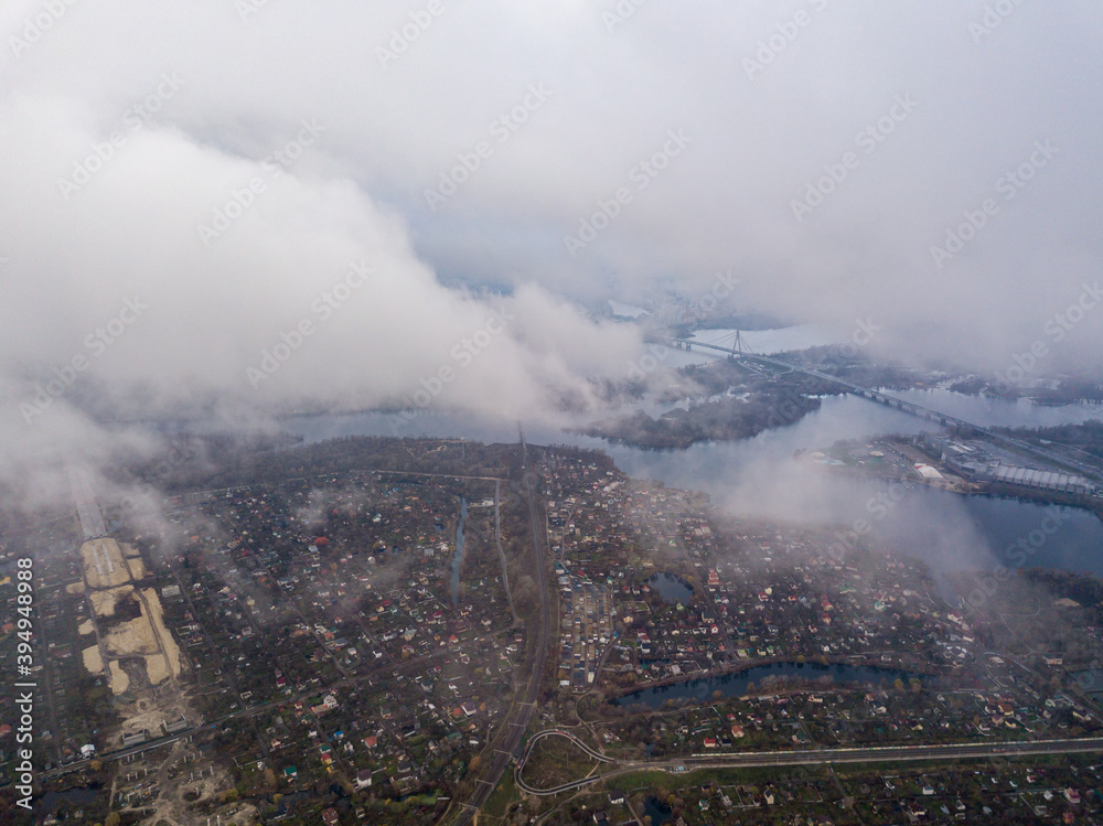 High aerial flight in the clouds over Kiev. An autumn cloudy morning, the Dnieper River is visible on the horizon.