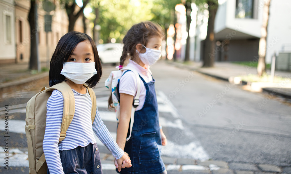 Small school girls with face mask outdoors in town, coronavirus concept.