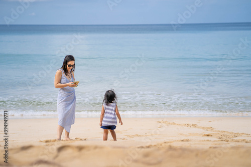 Young mother and daughter standing at sea shore against blue sky