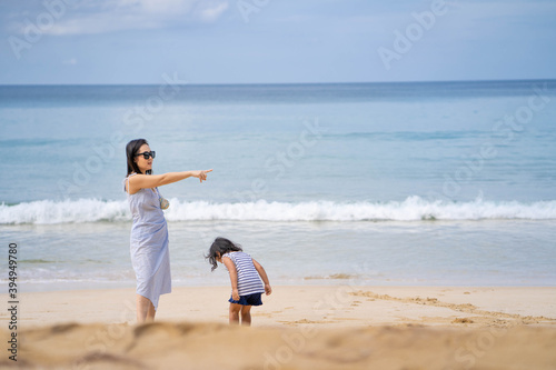 Young mother and daughter standing at sea shore against blue sky