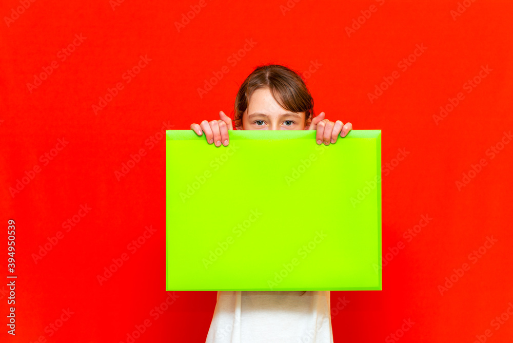 Young caucasian teenager girl holding blank paper sheet over red background.hiding face Young caucasian teenager girl holding blank paper sheet over red background.hiding face