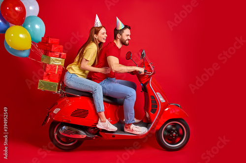nice beautiful couple on motorcycle bringing carrying bunch air balls festive decoration isolated over red studio background, making people happy