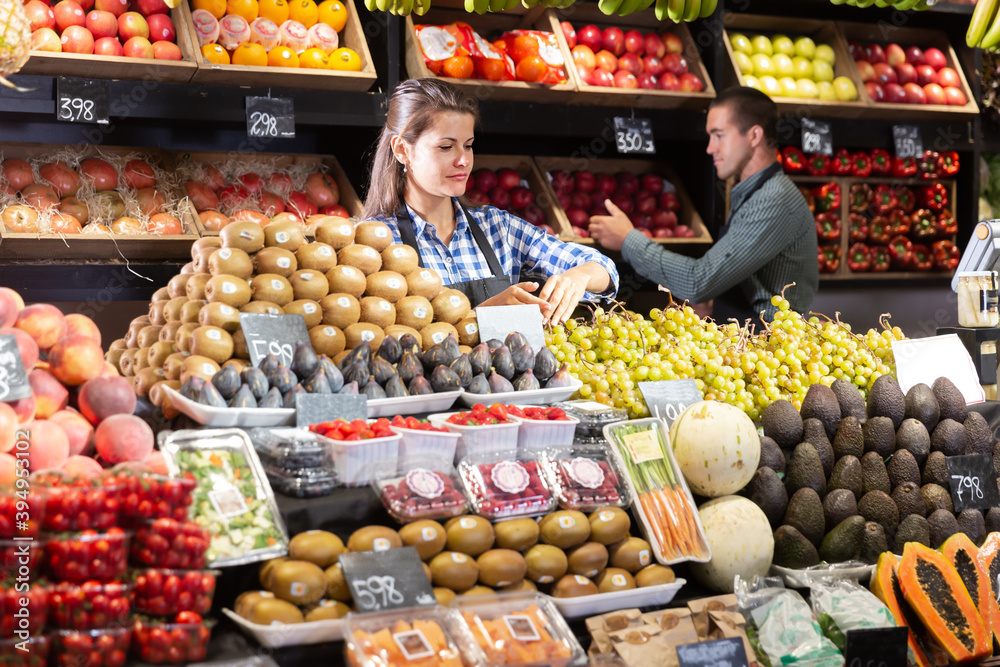 Friendly female shop assistant and man laying out vegetables in fruit and vegetable shop