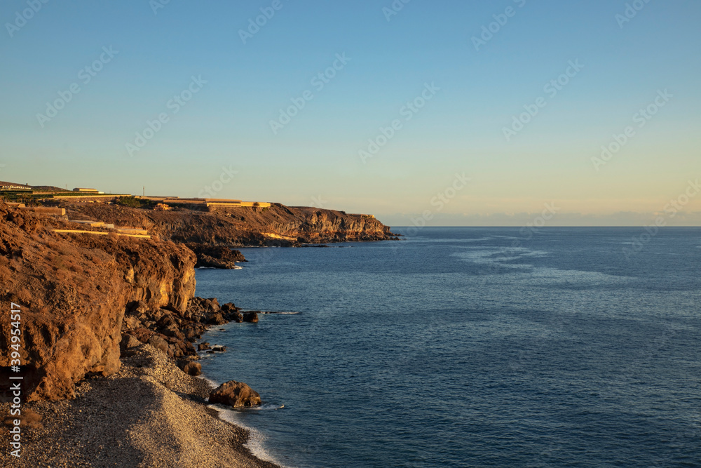 Wild beach near Playa San Juan at sunset, elevated views of the banana plantations on the top of the rough cliffs, familiar volcanic landscape of the western coast of Tenerife, Canary Islands, Spain