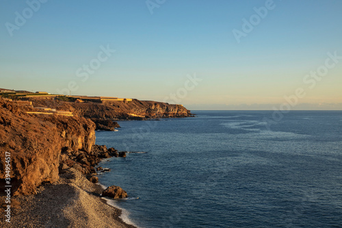 Wild beach near Playa San Juan at sunset, elevated views of the banana plantations on the top of the rough cliffs, familiar volcanic landscape of the western coast of Tenerife, Canary Islands, Spain © Ana