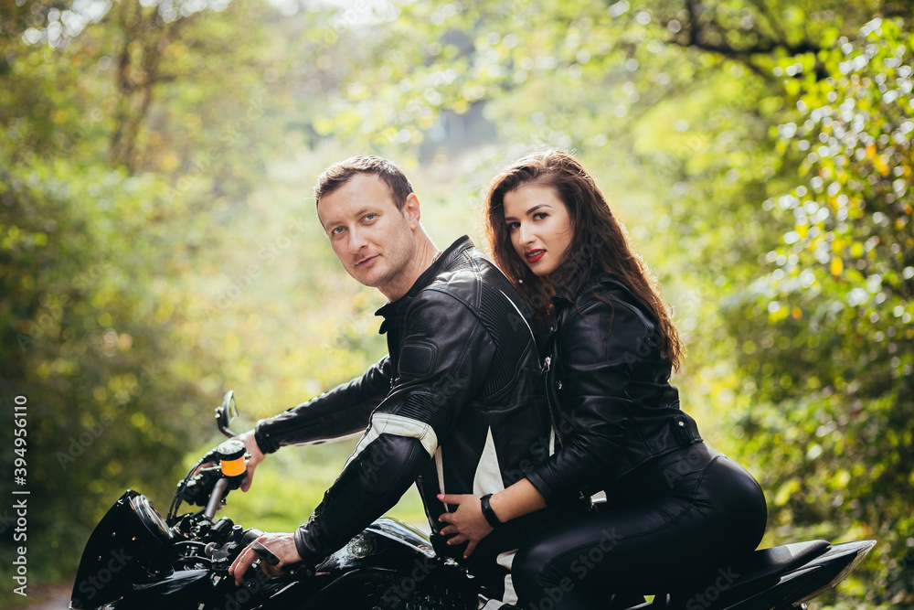Loving couple, guy and girl bikers, in black leather clothes. near a sports motorcycle on a forest road