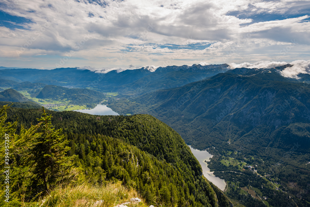 Standing on top of the mountain Planina Blato in the Triglav National Park in Slovenia with panoramic view over the Lake Bohinj and the village Stara Fužina on sunny day with clouds