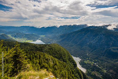 Standing on top of the mountain Planina Blato in the Triglav National Park in Slovenia with panoramic view over the Lake Bohinj and the village Stara Fužina on sunny day with clouds