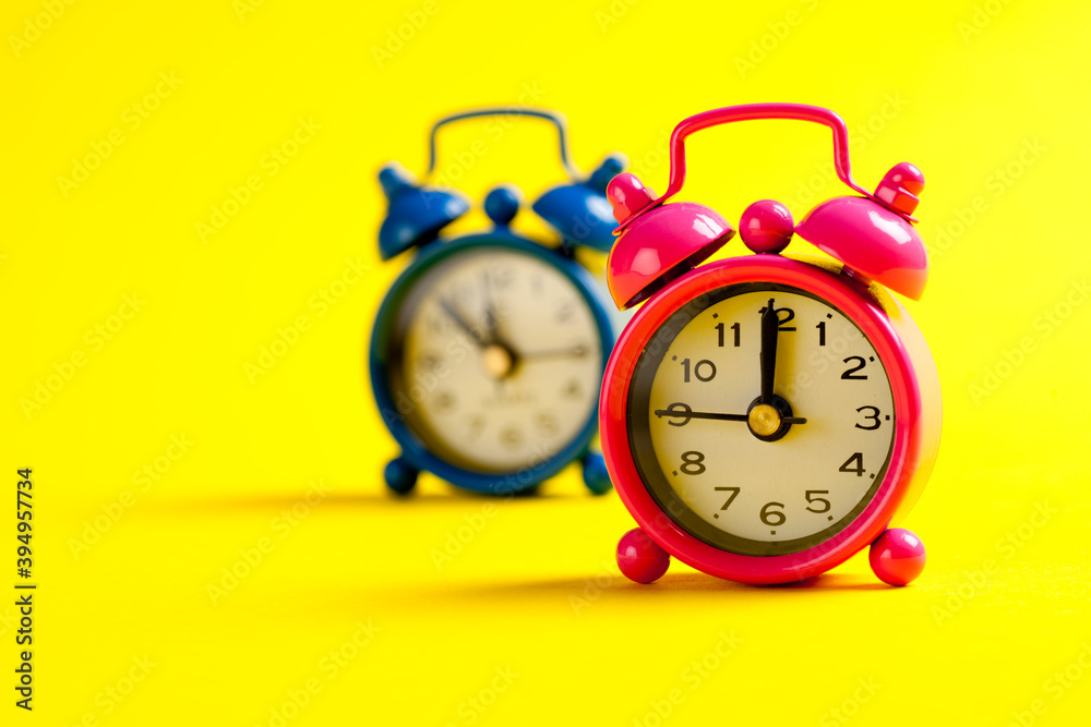 Studio photo of colorful miniature alarm clocks on yellow background, selective focus. Studio photo of colorful miniature alarm clocks on yellow background, selective focus.