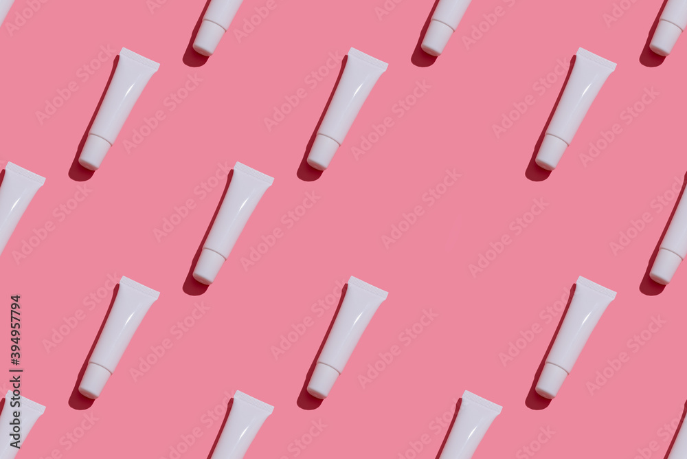 Obraz premium Trendy sunlight beauty pattern made with blank white tube lip gloss on bright light pink background, mock-up
