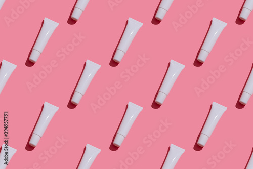 Trendy sunlight beauty pattern made with blank white tube lip gloss on bright light pink background,  mock-up