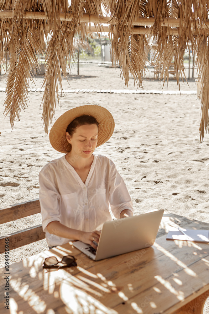 Young woman using laptop computer on a beach. Freelance work concept..Pretty young woman using laptop in cafe on tropical beach in outdoor cafe. Work and travel