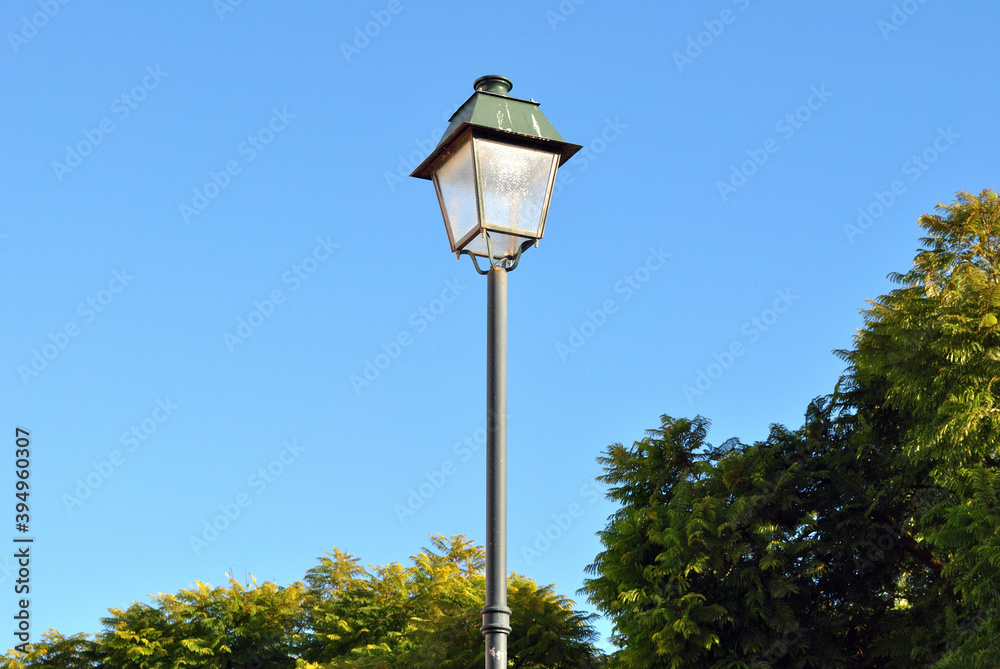 Isolated Steel Lamp Post seen against Blue Sky & Trees 