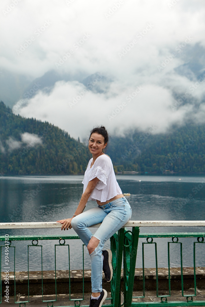 Fototapeta premium A girl in white clothing on a background of a mountain lake with blue water and mountains with clouds. Background.