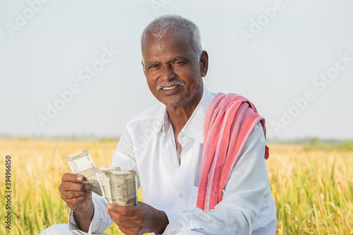 Happy smiling Indian farmer counting money on agriculture field while looking camera - concept of good or bumper crop harvest, farm subsidy and credit photo