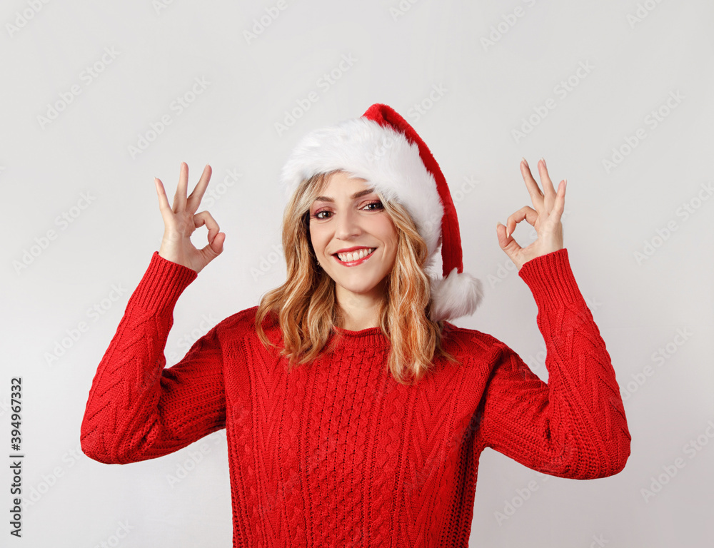 Young woman in santa hat smiling and doing okey sign Young woman in santa hat smiling and doing okey sign