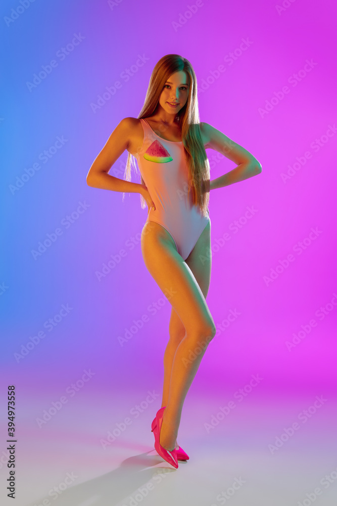 Long hair. Beautiful seductive girl in fashionable pink swimsuit on gradient purple-blue background in neon light. Full-length portrait. Copyspace for ad. Summer, fashion, beauty, emotions concept. Long hair. Beautiful seductive girl in fashionable pink swimsuit on gradient purple-blue background in neon light. Full-length portrait. Copyspace for ad. Summer, fashion, beauty, emotions concept.