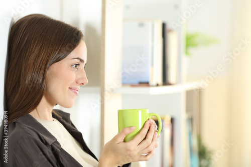 Satisfied woman holding coffee mug contemplating at home