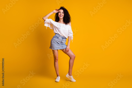 Full size photo of optimistic charming brunette woman standing hand on head wear white top blue skirt sneakers isolated on yellow background