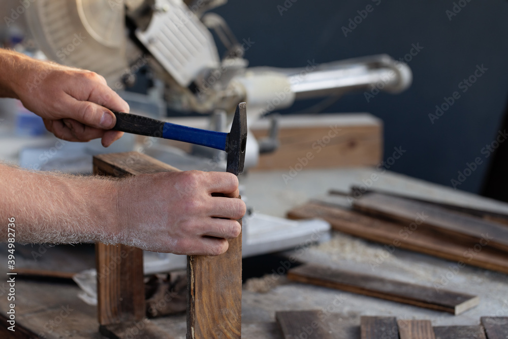 man hand is hammering nail on wood desk in workshop with construction background man hand is hammering nail on wood desk in workshop with construction background