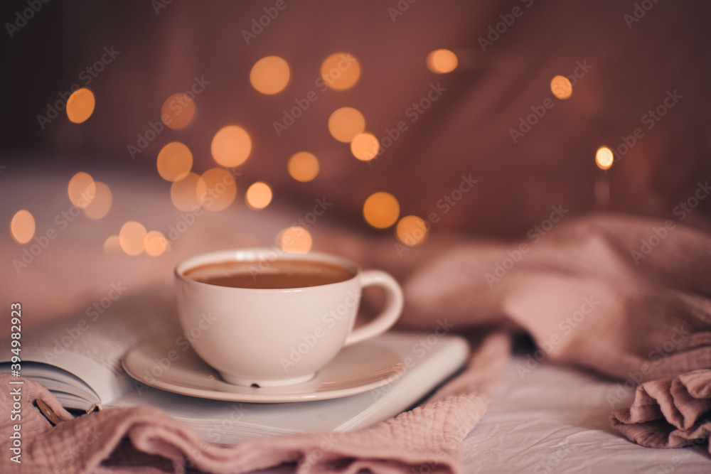 Fototapeta premium Tasty fresh cup of coffee on open paper book over Christmas lights close up. Good morning. Breakfast time. Winter holiday season.