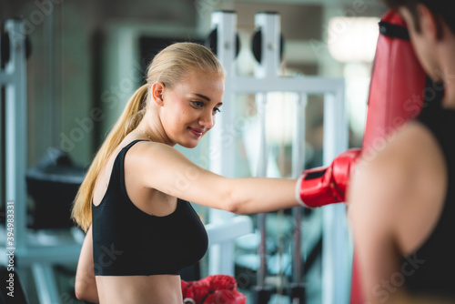 Strong young sportwoman exercising kick boxing and wearing gloves with trainer at fitness gym studio. Female and male fight. © chokniti