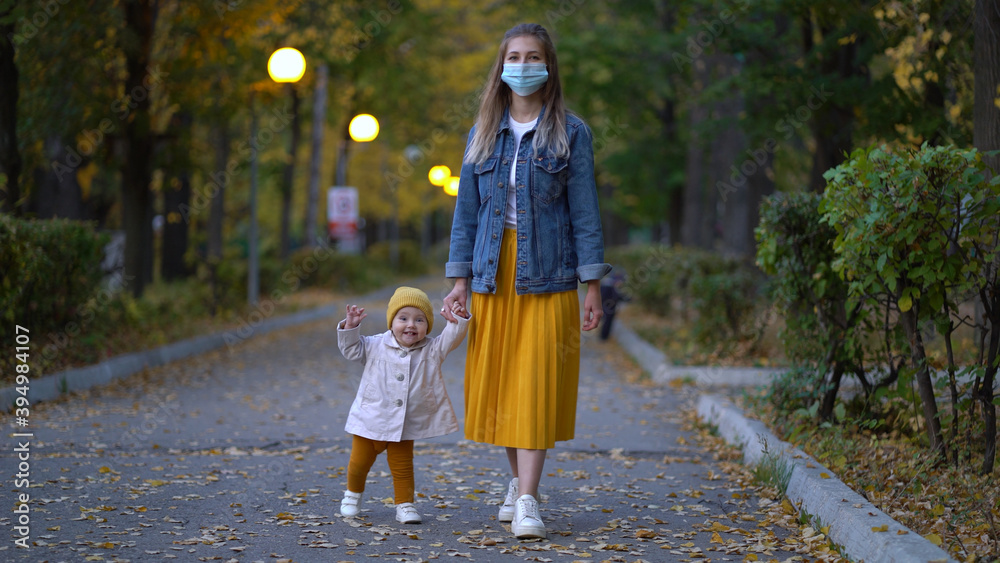 Masked mother holds hand lovely daughter on street walk during second wave quarantine coronavirus COVID-19 pandemic.