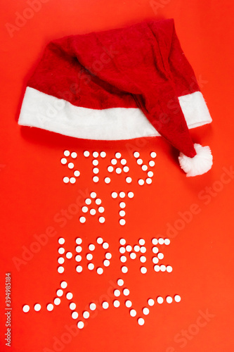 Stay home lettering from round white pills on a red background. Santa hat, face mask. High quality photo