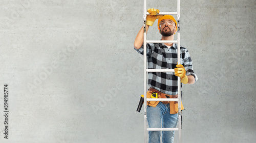 profession, construction and building concept - male worker or builder in helmet and gloves climbing up ladder over grey concrete background