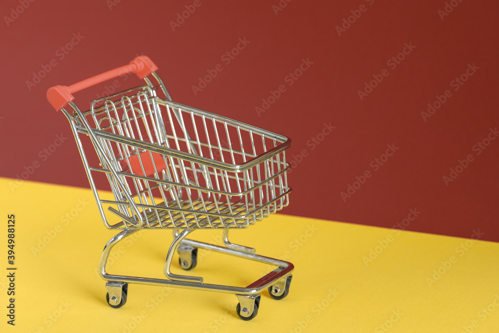Empty shopping cart on colorful yellow and brown background. Online shopping or e-commmerce concept. Copy space, banner.