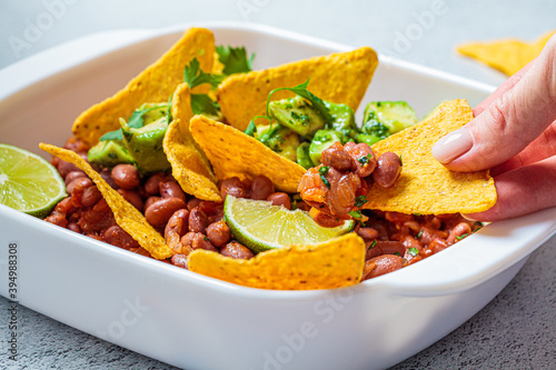 Bean salad with avocado and nachos in white dish, gray background. Mexican food concept.