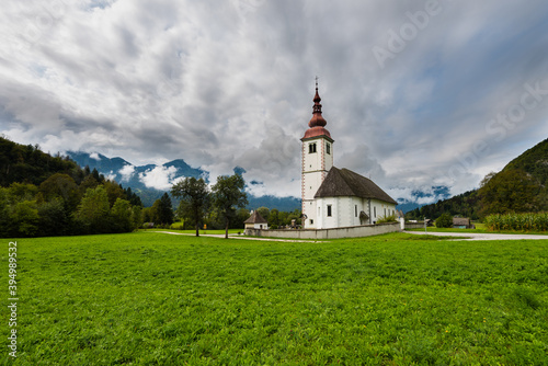 Beautiful old solitary church with adjacent cemetary in mountain valley with fresh grass and cloudy sky amidst high mountain peaks