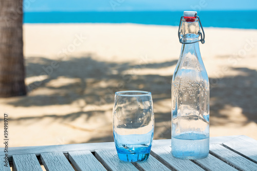 Glass bottle with glass on the table overlooking the sandy seashore.